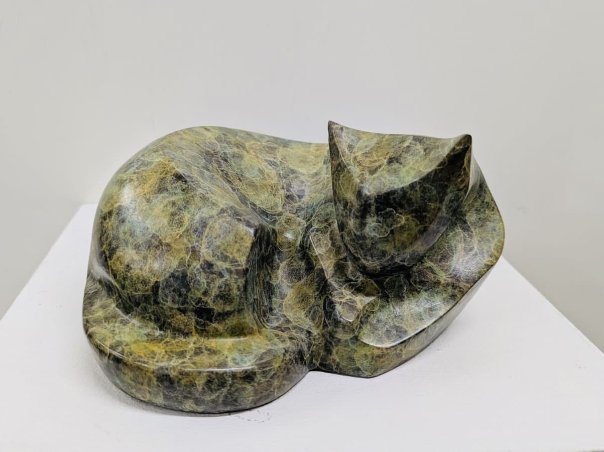 Bronze cat sculpture resting peacefully in the sunshine by Marie Ackers, capturing feline tranquillity and relaxation.