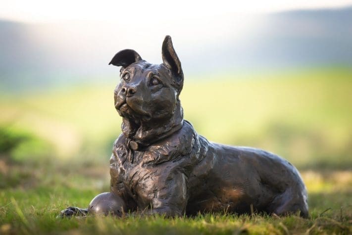 Bronze sculpture of a lying crossbreed dog with ball by Tanya Russell