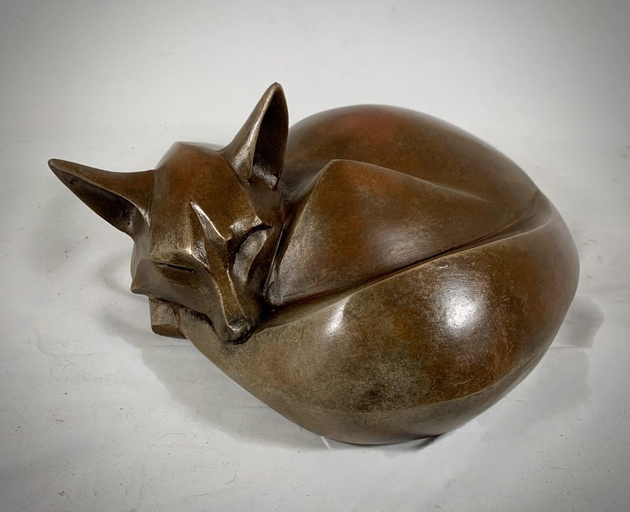 Bronze resin fox sculpture by Marie Ackers depicting a curled fox resting peacefully.